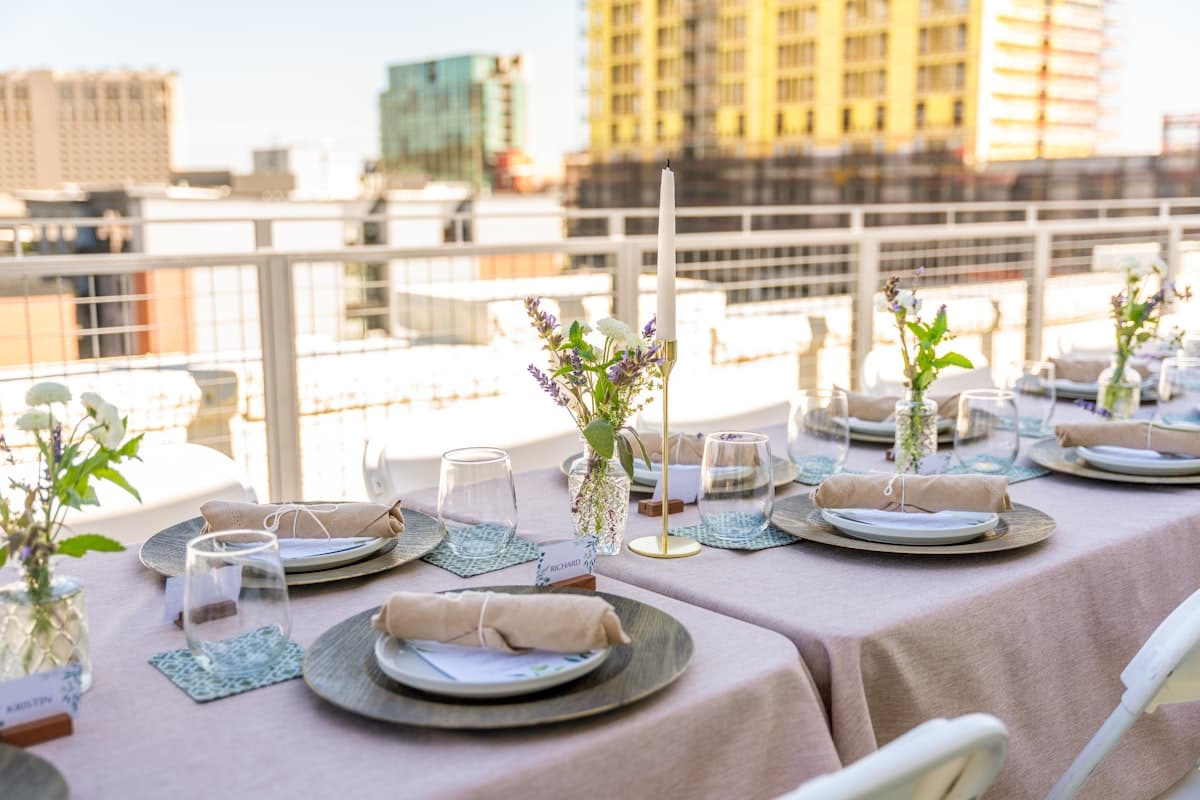 A rooftop dinner table with wine, candles, and plated dishes at dusk